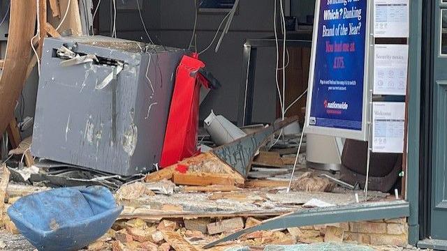 The damaged front of Nationwide, showing a grey box on the floor, broken bricks, damaged signs, and cabled hanging down.