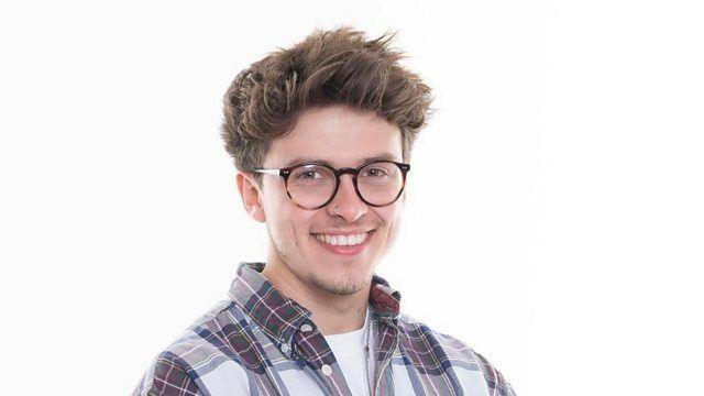 A head and shoulders image of Connor Bennett. He is wearing a shirt over a white T-shirt and glasses. He is standing against a white backdrop and smiling.