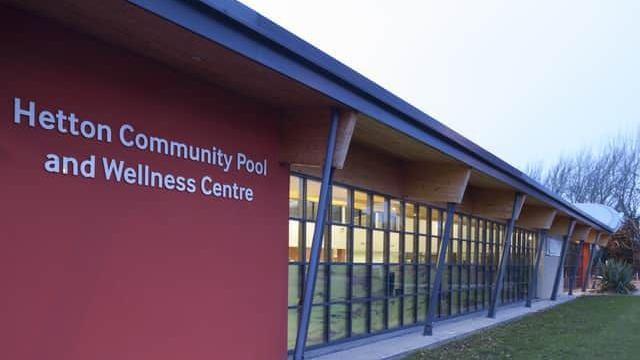 Hetton Community Pool and Wellness Centre. It is a red building with a lot of windows, and a lawn surrounding it.