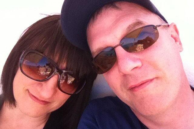 Chris and Rita pictured together. Rita had short brown hair and was wearing brown sunglasses. Chris was wearing a blue baseball cap and sunglasses