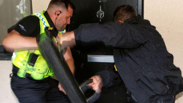 A uniformed police officer and a detective break down a door during a raid in Rochdale