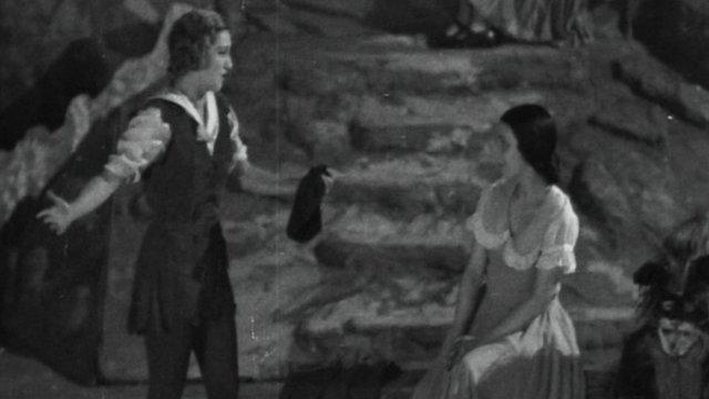 Dorothy Dickson, in costume as Dick Whittington, singing a love song to "Alice", played by Jean Adrienne, as part of a pantomime at the Garrick Theatre in 1932
