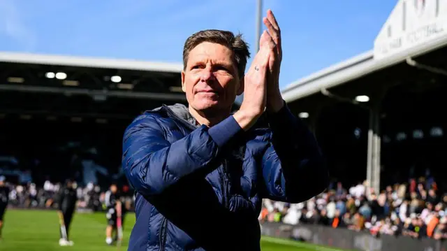 Wearing a blue jacket, a serious-looking Oliver Glasner claps on the pitch at Craven Cottage