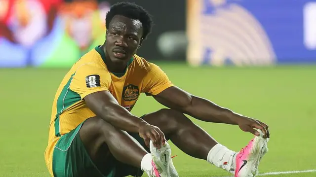 Nestory Irankuda sits on the turf in his Australia kit