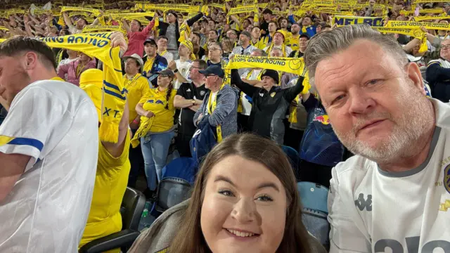 An image of a father and daughter posing for a selfie among hundreds of Leeds United scarves