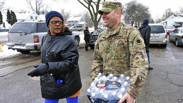 Michigan National Guard Sgt. Steve Kiger of Harrison, Mich., carries water for a resident, Wednesday Jan 13, 2016 in Flint, Mich