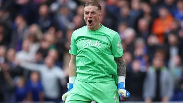 Jordan Pickford, wearing green Everton goalkeeper kit, clenching his fists and shouting towards his team-mates