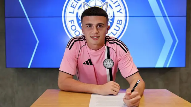 A smiling Jake Evans signs his first professional contract with Leicester sitting at a table.