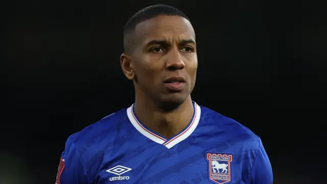 Ashley Young, wearing Ipswich Town's blue home shirt with a white collar and red and blue trim. The shirt has an Umbro logo on one side and Ipswich crest on the other.