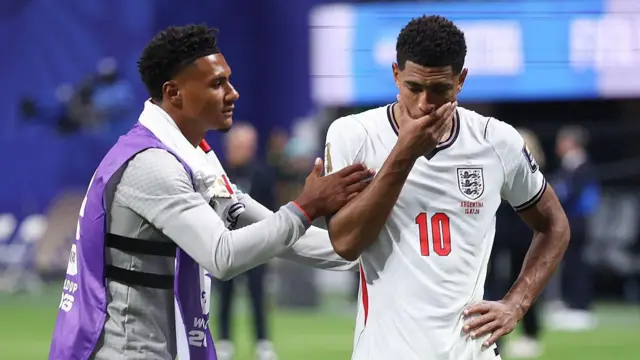 Ollie Watkins, wearing a substitute's bib, consoles Jude Bellingham on the pitch after England lost to Argentina at the World Cup