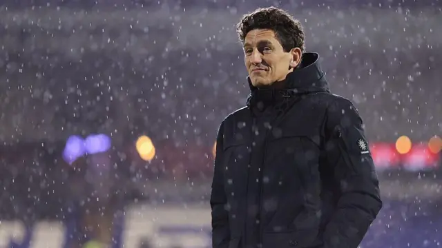 Keith Andrews, wearing a dark winter coat, stands in the pouring rain looking pensive