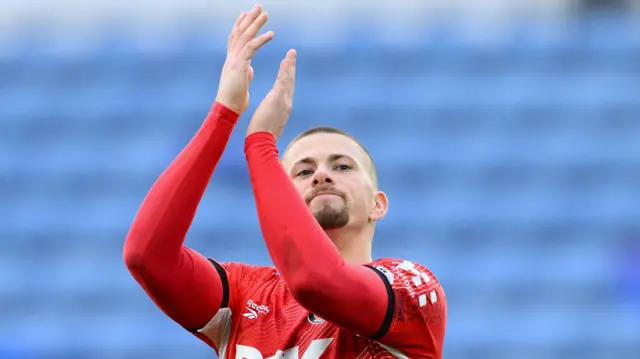 Harry Clarke applauds Charlton Athletic fans while wearing a red home shirt with a long-sleeved red top underneath