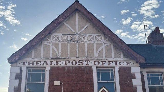 The photograph shows an original Theale Post Office logo just below the roof line of the current post office on the village's High Street.