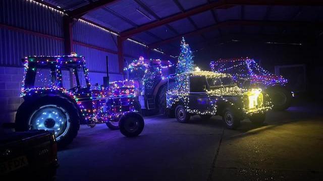 Brightly lit tractors and a farm vehicle are parked in a dark barn before heading out on the parade 