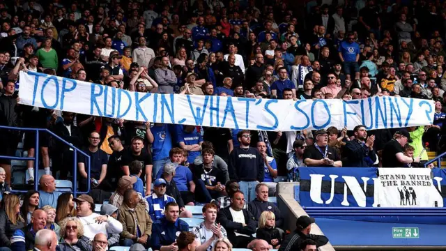 Fans hold up a message to the chairman and director of football, reading: "Top Rudkin, what's so funny?"