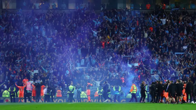 Coventry players celebrate with their travelling fans at Blackburn after securing promotion, with blue smoke from a flare drifting across the pitch from the stands