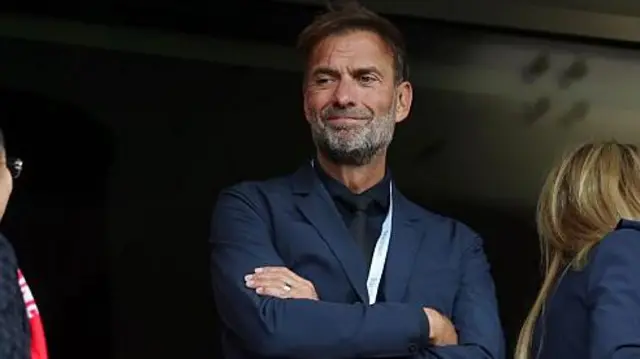 A smiling Jurgen Klopp stands with his arms folded in the Main Stand at Anfield