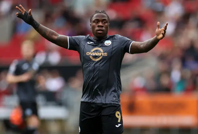 Michael Obafemi, wearing a black Swansea change kit, with arms outsretched