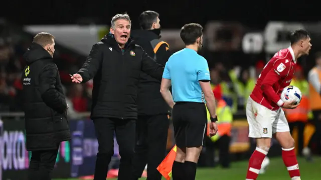 Phil Parkinson standing on the touchline with his arms outstretched and his mouth open saying something to the assistant referee who is stood infront of him.