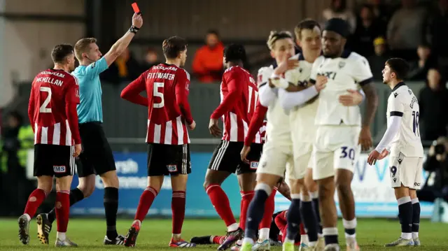 The referee shows Oxford midfielder Tyler Goodrham a red card in the FA Cup third-round game at Exeter