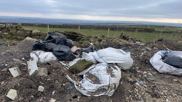 Large bags of rubbish and building waste dumped near a field.