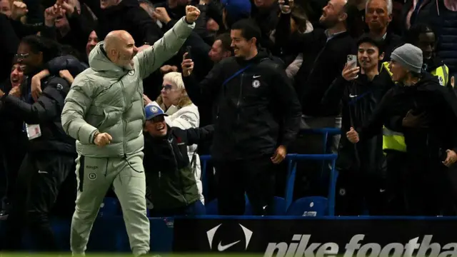 Enzo Maresca punches the air towards the crowd, with supporters celebrating in the background