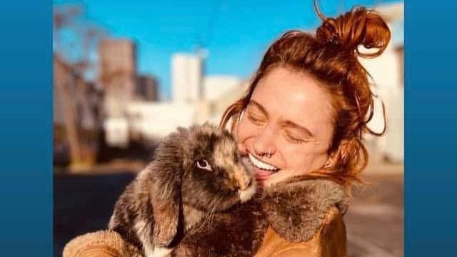 Eleanor Thompson cuddles a lop-eared rabbit, smiling broadly. She wears a brown coat with a fur collar, with her red hair piled up on her head.