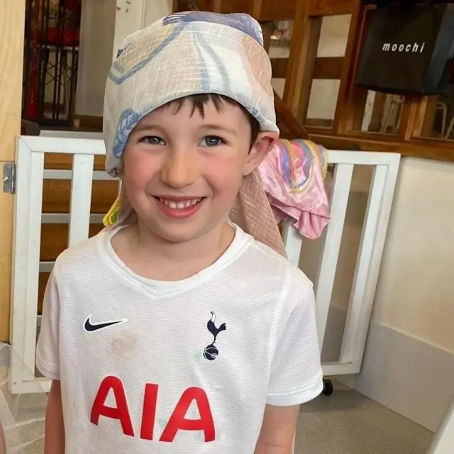A picture of a boy in a Tottenham shirt with a headdress and a girl in a yellow dress holding a baby