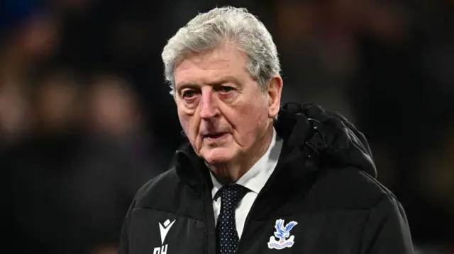 Roy Hodgson wearing a dark Crystal Palace coat with an eagle on it over a white shirt and spotted tie