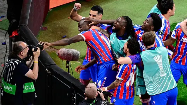 Crystal Palace celebrate their goal in the Europa Conference League final. Players mob Mateta. Mateta tries to grab a photographer's camera.