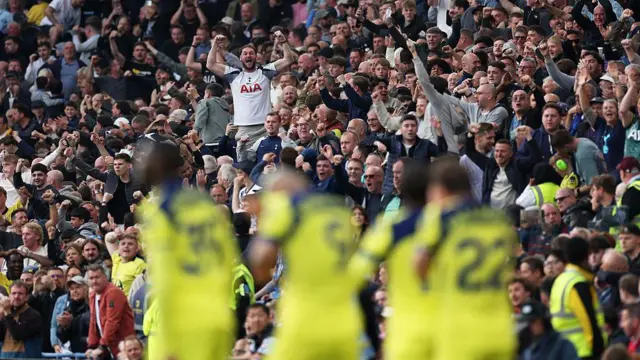 Blurred Spurs players celebrate Conor Gallagher's goal in the foreground while Spurs supporters celebrate in the background