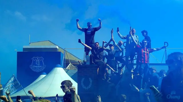 Fans climb up onto the posts to set off blue flares 