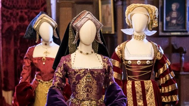 Three ornate Tudor dresses are displayed on manikins with white, empty faces.