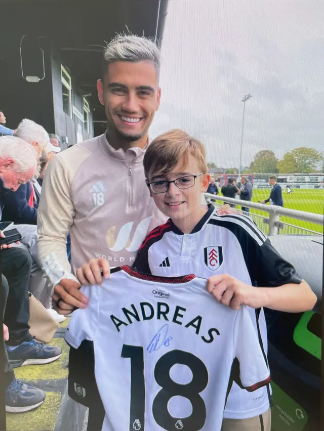 A young boy holds a signed Fulham shirt alongside Andreas Pereira