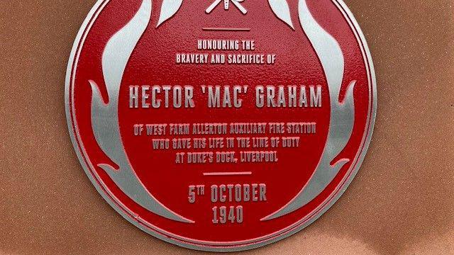 A close up of the red circular plaque which has embossed silver writing which reads: Honouring the bravery and sacrifice of Hector 'Mac' Graham of West Farm Allerton Auxiliary Fire Station who gave his life in the line of duty at Duke's Dock, Liverpool - 5th October 1940