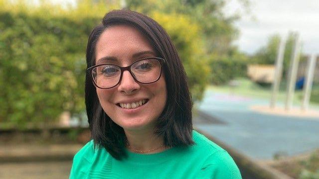 Judith Divers smiling into the camera. She has glasses, a green top and black hair in a bob.