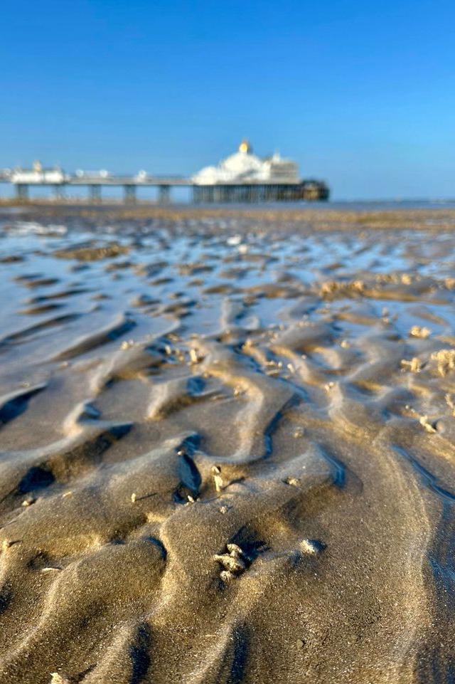 Wet sand with a pier blurred in the background 