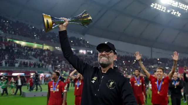 Jurgen Klopp holds up Club World Cup trophy towards supporters with several Liverpool players out of focus in the background
