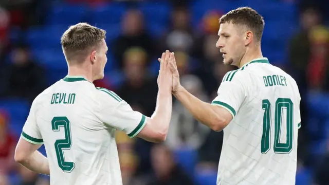 Terry Devlin and Jamie Donley celebrating Donley's goal for Northern Ireland in the international side's white and green away kit