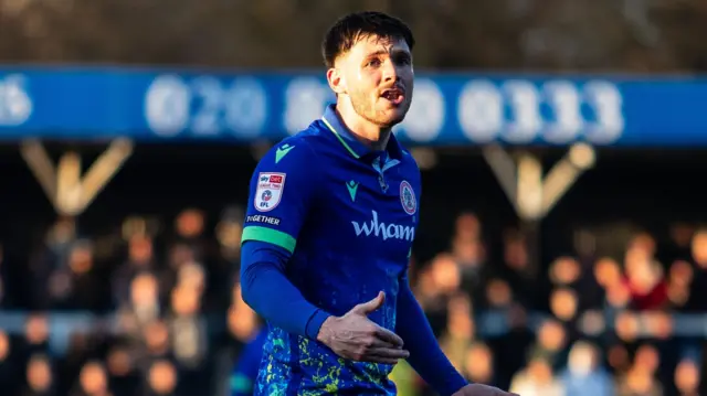 Freddie Sass standing on the pitch wearing Accrington Stanley's blue kit during a game in the 2025-26 season