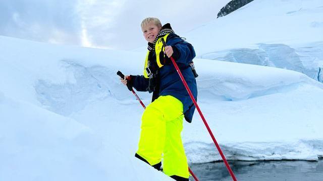 Jamie with blond hair wearing skiing clothes smiling as he uses red walking poles in the snow in Antarctica 