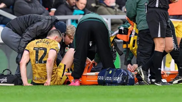 Lewis Miller (left) sat on the floor with a stretcher next to him and medical staff attending to him