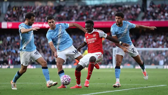 Bukayo Saka of Arsenal controls the ball while under pressure from Bernardo Silva, Rodri and Matheus Nunes of Manchester City