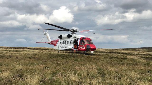 A red and white coastguard helicopter sat on rolling Derbyshire moorland with ominous dark clouds gathering above