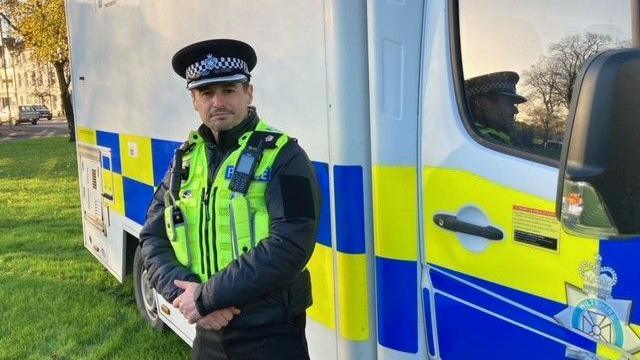 man in police uniform stands in front of police van parked on grass