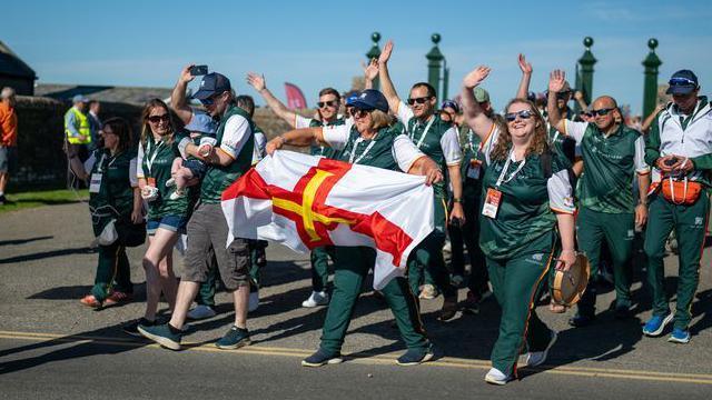 The Guernsey team at the opening ceremony of the 2025 Island Games, waving and holding a flag.