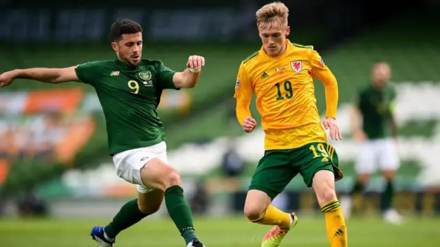 Matt Smith in a yellow Wales shirt controls the ball under pressure from the Republic of Ireland's Shane Long
