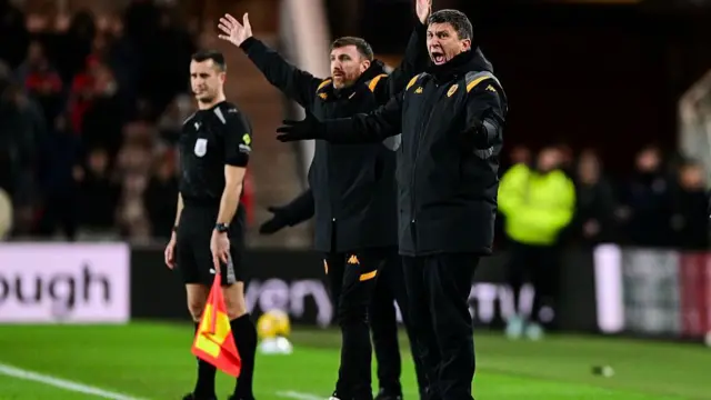 Marco Salatovic stands on touchline with arms up in the air appealing to officials, alongside head coach Sergej Jakirovic who is roaring his displeasure as an assistant referee stands in background