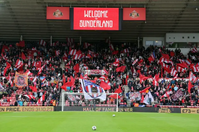 Fans and a flag display at the Stadium of Light with 'Welcome to Sunderland' on the display board above the stand.