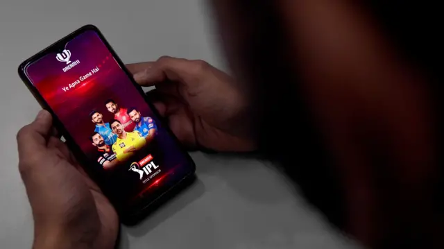 In this photo illustration taken on October 12, 2020, a user checks the Dream11 application of the Indian Premier League (IPL) cricket tournament, on his mobile phone in New Delhi. Unable to bet legally, tens of millions of Indian cricket fans have turned to fantasy games based on the Indian Premier League, which have exploited a loophole to create a billion-dollar industry